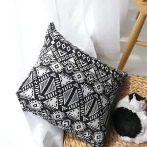Ethnic geometric black and white jacquard cushion cover on woven mat with soft light