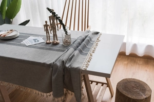 Close-up of grey striped cotton linen tablecloth with decorative tassel fringes on edge