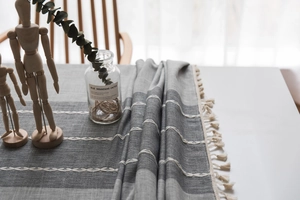 Close-up of grey embroidered table runner with cotton linen texture and white tassels