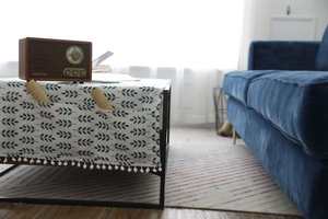 Détail de nappe en lin nordique avec motif feuilles, poche latérale et pompons blancs