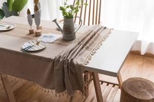 Detail view of linen-textured table runner with white stripes and elegant beige tassels