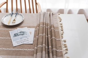 Close-up of linen-textured table runner featuring wavy embroidery and fringe tassels