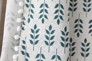 Détail macro d'une nappe nordique en lin avec motifs de feuilles vertes et pompons blancs