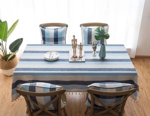 Détail de la nappe à rayures bleues avec franges à glands et coussin à carreaux assorti