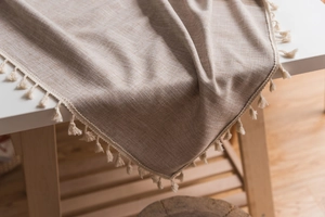 Detail of beige cotton linen tablecloth featuring tassel fringe and woven texture