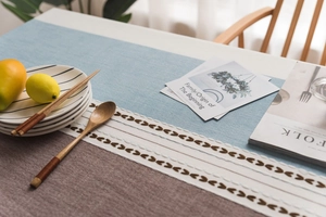 Detail of Nordic linen style tablecloth with blue embroidery and elegant lace fringe