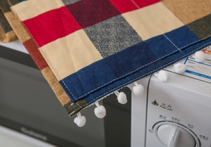 Detail of plaid cotton linen microwave cover with white pom-pom trim and fabric texture