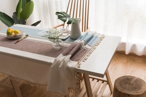 Detail of Nordic table runner with cotton linen patchwork design and white tassel fringe