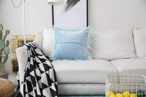 Detail view of a light blue faux wool pillow cover with mint green plush fringe on a sofa