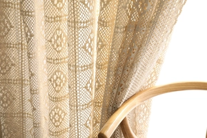 Gros plan d'un rideau en dentelle crochetée beige avec motifs floraux et lumière douce