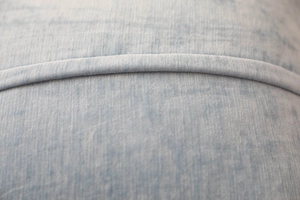 Close-up of light blue fabric texture with refined piping detail on the cushion cover