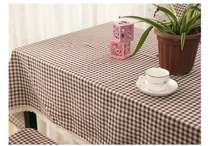 Detail van een bruin geruit linnen tafelkleed met een witte kanten rand op een houten tafel
