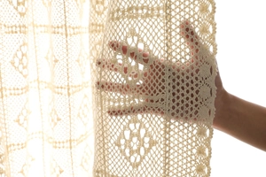 Détail macro du rideau en dentelle crochet crème montrant les motifs semi-transparents