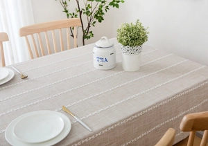 Close-up detail of beige linen tablecloth with white linear embroidery and textured fabric