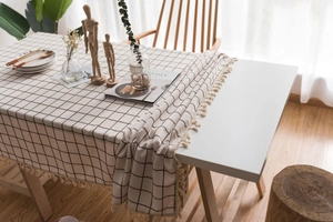 Close-up of minimalist beige plaid tablecloth featuring elegant tassel edges and linen texture