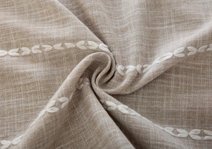 Macro detail of beige linen fabric featuring elegant white leaf embroidery texture