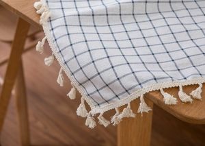 Detail of Mediterranean blue checkered tablecloth with elegant fringe tassels on wooden table