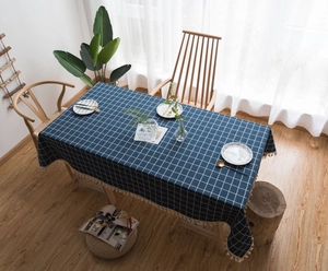Detail of dark blue checkered tablecloth with beige tassels on a rectangular wooden table