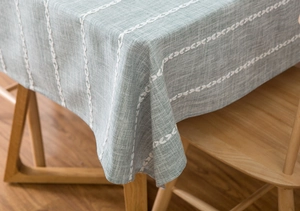 Detail of light green cotton linen tablecloth with white leaf embroidery on wood table