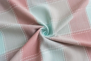 Close-up of green and pink plaid fabric with lace embroidery and soft spiral folds
