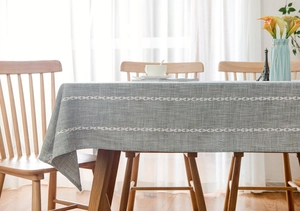 Close-up of grey-blue linen tablecloth with white leaf embroidery on a wooden table