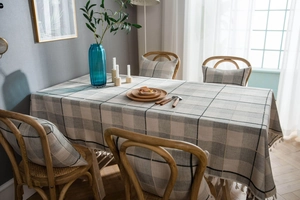 Close-up of grey plaid linen tablecloth with elegant white tassels and matching cushion