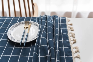 Detail of navy blue plaid tablecloth with decorative cream tassels and textured fabric