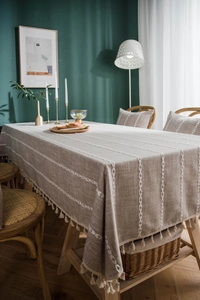 Detail of linen tablecloth featuring white embroidered leaves and elegant cream fringes