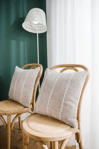 Detail of oatmeal linen pillow cover with white chain embroidery on a woven chair