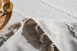 Close-up of beige linen tablecloth featuring white chain embroidery and tassel edge details