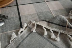 Macro detail of gray plaid linen tablecloth featuring white tassel fringe and fabric texture
