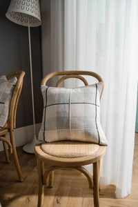 Detailed close-up of grey plaid linen cushion with cross-stitch sewing on a wooden chair