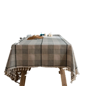 Gray and beige plaid tablecloth with white tassels on a rustic wooden dining table
