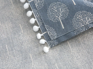 Detail of grey-blue linen fabric with white tree patterns and decorative pom-pom trim