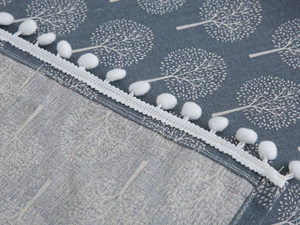 Detail of grey-blue dust cover fabric with white tree patterns and white pom-pom trim edge