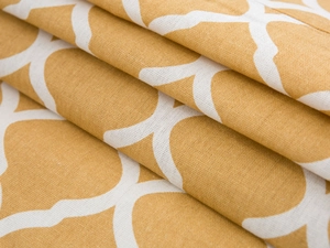 Close-up of mustard yellow fabric with white geometric clover patterns and woven texture