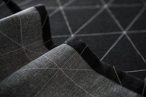 Macro detail of dark grey linen tablecloth with white geometric grid and sewn edge
