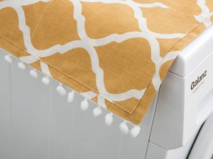 Close-up of yellow geometric dust cover with white pom-poms on top of a washing machine