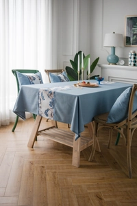 Detailed close-up of blue floral embroidery on rustic linen-style tablecloth and pillow