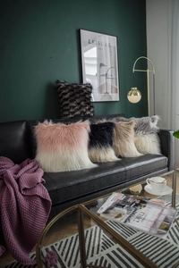 Detail of five faux fur cushion covers in various colors on a black leather sofa
