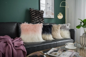Detail of plush faux sheepskin pillow covers in gradient colors on a black leather sofa