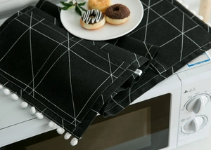 Detailed view of black and white geometric microwave cover with stylish pom-pom fringe