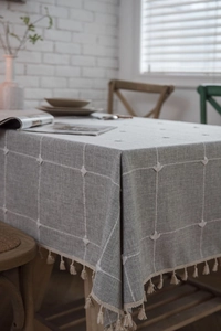 Detailed view of gray linen tablecloth with white grid embroidery and tassel edges