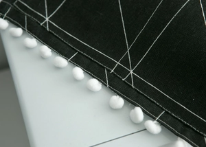 Close-up of black microwave oven cover with white geometric lines and pom-poms edge
