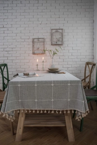 Close-up of grey plaid tablecloth with elegant cream fringe edges on a wooden dining table