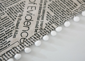 Detail view of cotton linen dust cover with vintage newspaper print and white pom-poms