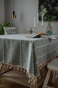 Close-up of Morandi green linen tablecloth featuring white cross-stitch and tassel trim