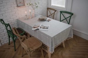 Close-up of light grey checkered linen tablecloth with embroidered floral details and tassels