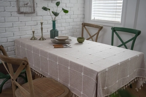 Detail of grid embroidered linen tablecloth with decorative white tufts and fringe edges