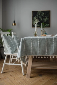 Detail of coffee-colored linen tablecloth featuring white leaf embroidery and beige tassels